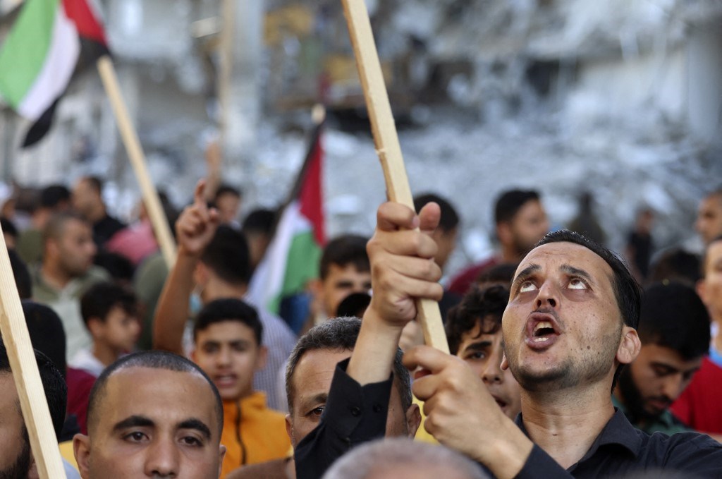 فلسطينيون يسيرون أمام المباني التي دمرتها الغارات الإسرائيلية في غزة 15 حزيران / يونيو 2021 (أ ف ب).