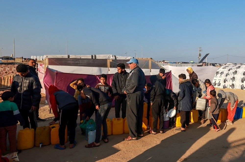 نازحون فلسطينيون يصطفون للحصول على المياه في مخيم موقت في رفح بالقرب من الحدود مع مصر (أ ف ب)