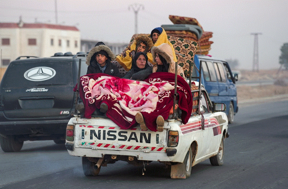 نازحون أكراد سوريون يركبون في الجزء الخلفي من سيارة محملة بممتلكاتهم على طريق حلب - الرقة السريع 