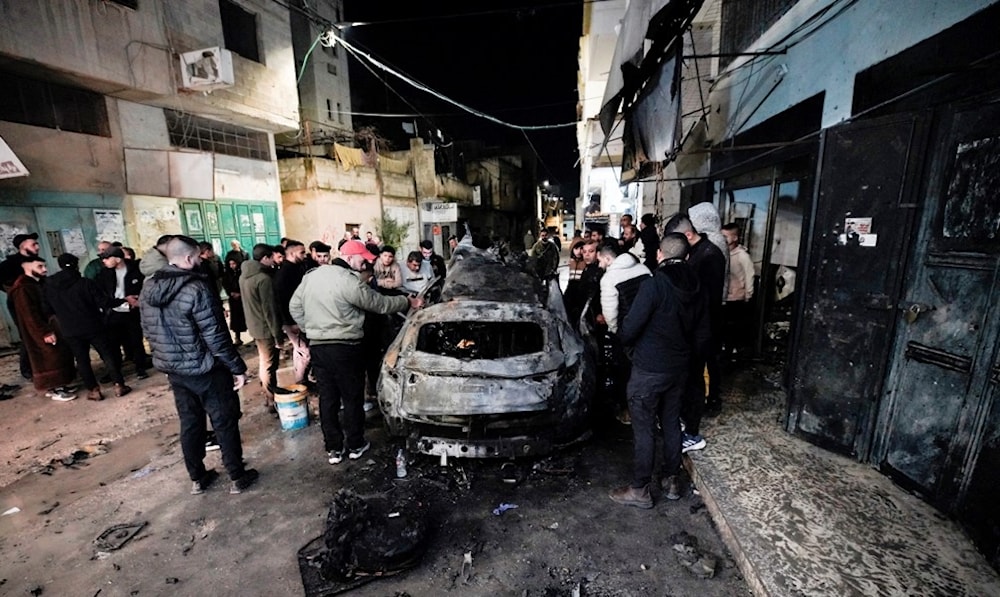 فلسطينيون يتفقدون السيارة المستهدفة في مخيم جنين - 22 شباط/فبراير 2024 (أ ف ب)