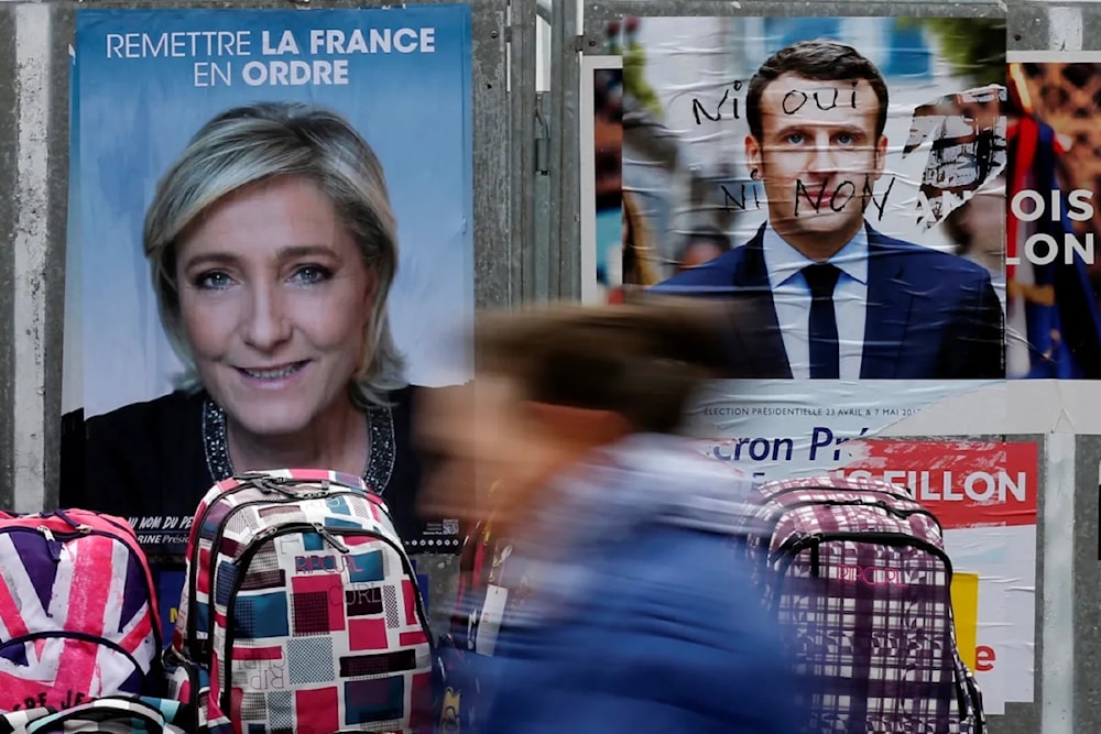 امرأة تمرّ أمام ملصقات حملة انتخابية سابقة لمارين لوبان وإيمانويل ماكرون في باريس (وكالات)