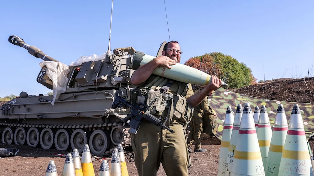 جندي إسرائيلي يحرك قذيفة مدفعية بالقرب من مدفع هاوتزر ذاتي الدفع 