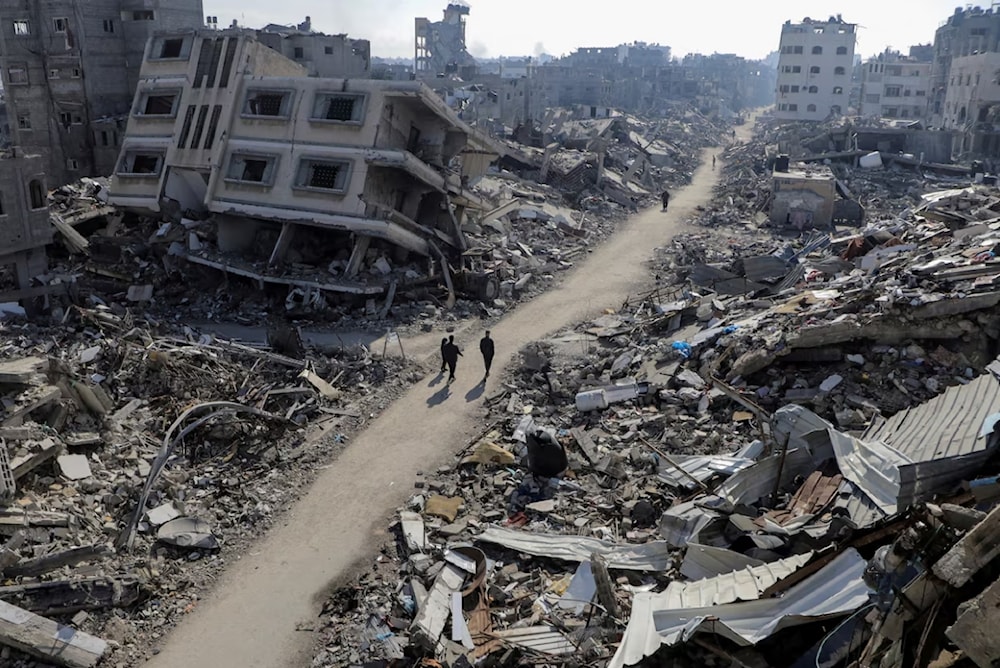 فلسطينيون يسيرون بين المنازل المدمرة في مخيم جباليا شمالي قطاع غزة في شباط/فبراير الماضي (رويترز)