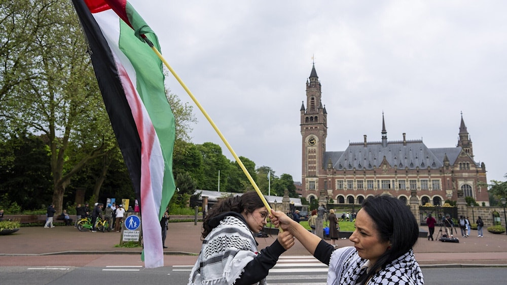 متظاهرتان تلوحان بالعلم الفلسطيني أمام قصر السلام الذي يضم محكمة العدل الدولية في لاهاي. (AP)