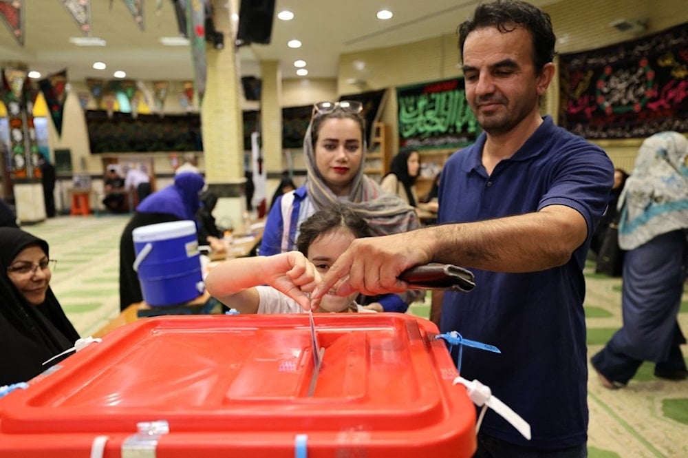 طفلة تساعد والدها في الإدلاء بصوته في مركز اقتراع في طهران، في الجولة الثانية من الانتخابات الرئاسية الإيرانية (أ ف ب)