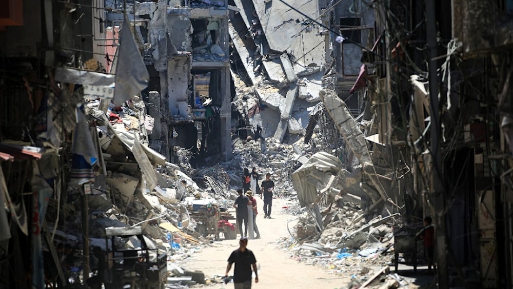 رجال فلسطينيون يسيرون في شارع ضيق بجوار المباني المدمرة في خان يونس جنوبي قطاع غزة (أرشيف)