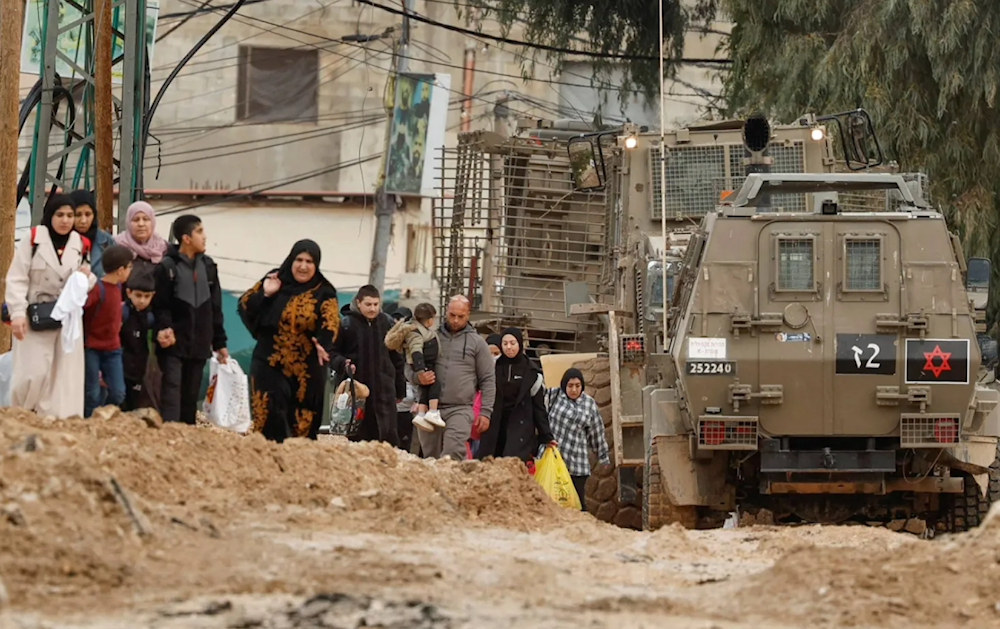 فلسطينيون يسيرون بجوار آليات عسكرية أثناء مغادرتهم مخيم جنين في الضفة الغربية أمس (رويترز)