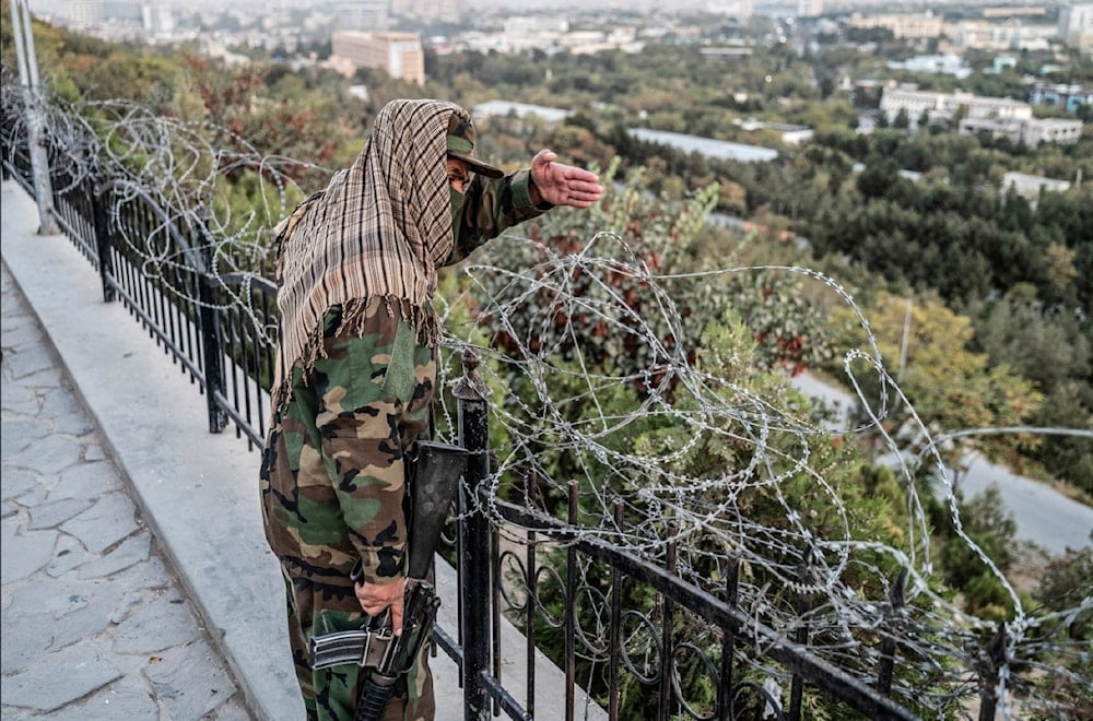 أحد أفراد أمن طالبان يشير من خلف الأسلاك الشائكة في أثناء وقوفه حارساً على قمة تل وزير أكبر خان في كابول (أ ف ب)