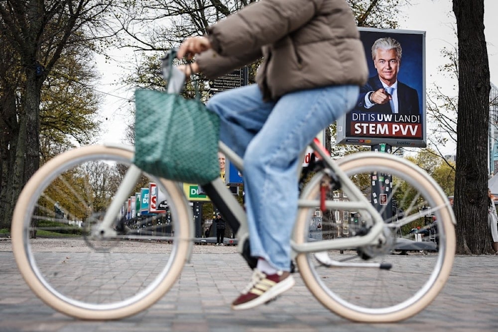 مواطن هولندي يمر بدراجته بجانب لوحة دعائية لرئيس حزب الحرية اليميني المتطرف، خيرت فيلدرز، في لاهاي (29 أكتوبر 2025 - أ ف ب)
