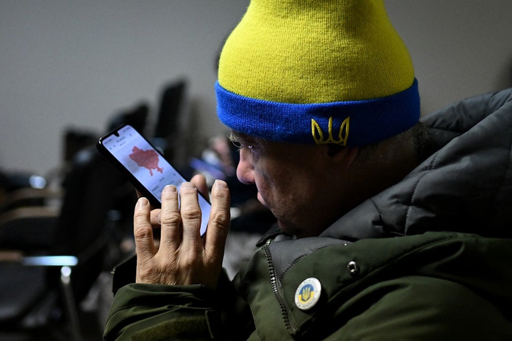رجل أوكراني يتحقق من خريطة تنبيه الغارات الجوية على هاتفه أثناء جلوسه في ملجأ فندق تحت الأرض خلال هجوم جوي في كييف - 25 تشرين الثاني/8نوفمبر 2025 (أ ف ب)