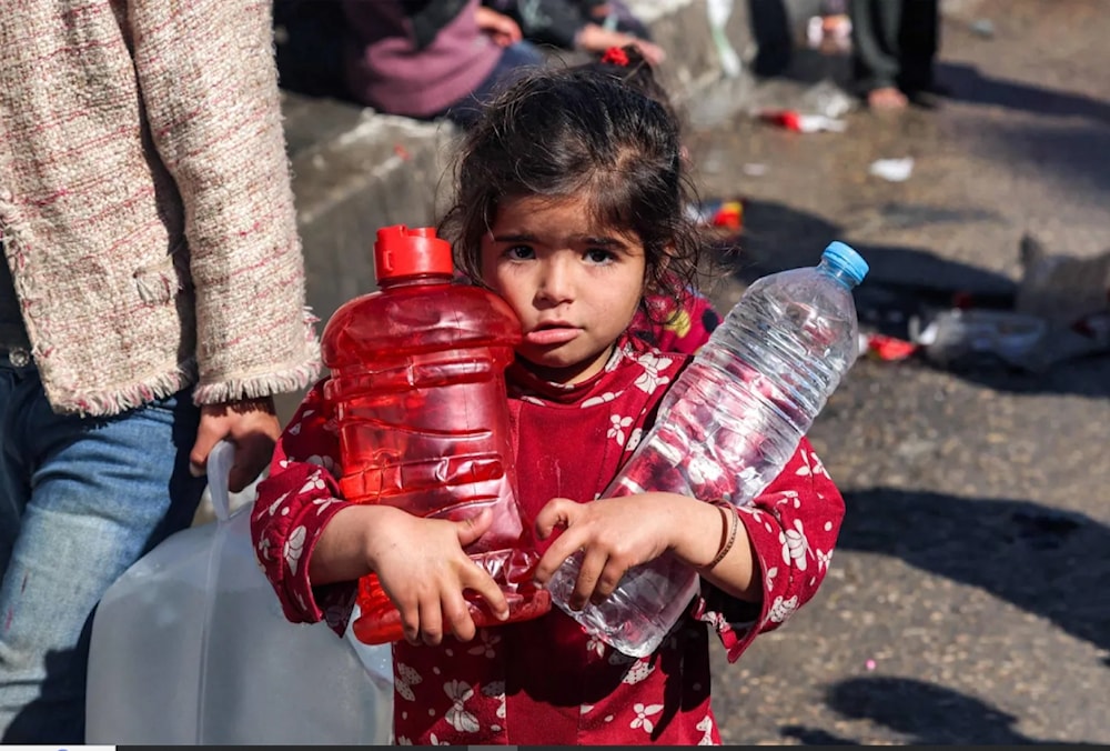 فتاة تحمل زجاجات بلاستيكية مملوءة بالمياه في أحد شوارع مدينة رفح جنوب قطاع غزة (أ.ف.ب)