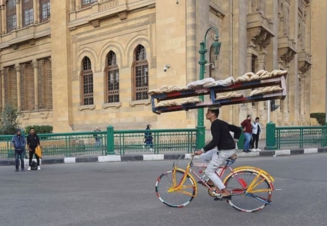 بائع متجول مصري يركب دراجة هوائية ويحمل الخبز على رفوف خشبية في القاهرة في مصر