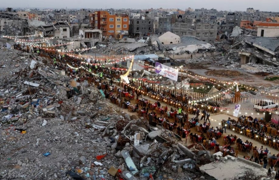 فلسطينيون بتناول وجبات الإفطار خلال شهر رمضان المبارك، بالقرب من أنقاض المباني، في رفح. قطاع غزة. 1 آذار/مارس 2025. (رويترز)