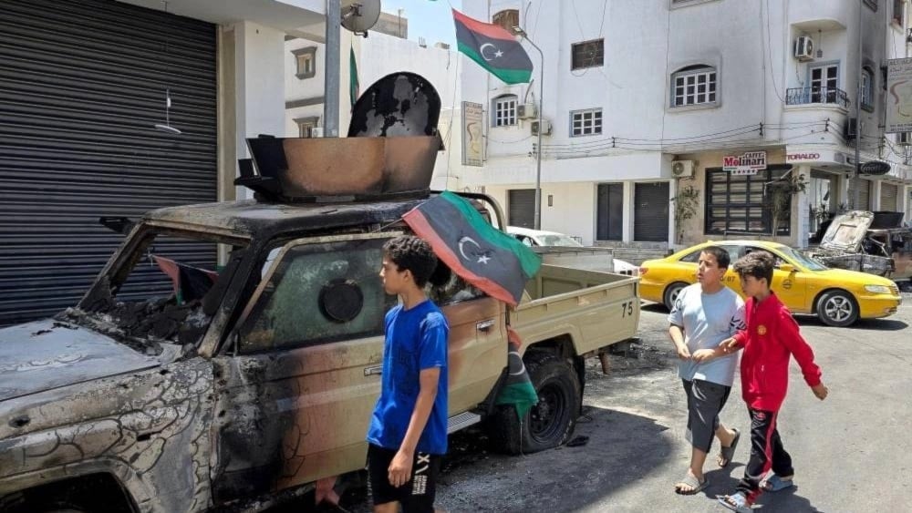 أطفال يمرون من أمام سيارة مدمرة عقب اشتباكات ليلية في حي أبو سليم جنوبي طرابلس (أ ف ب)