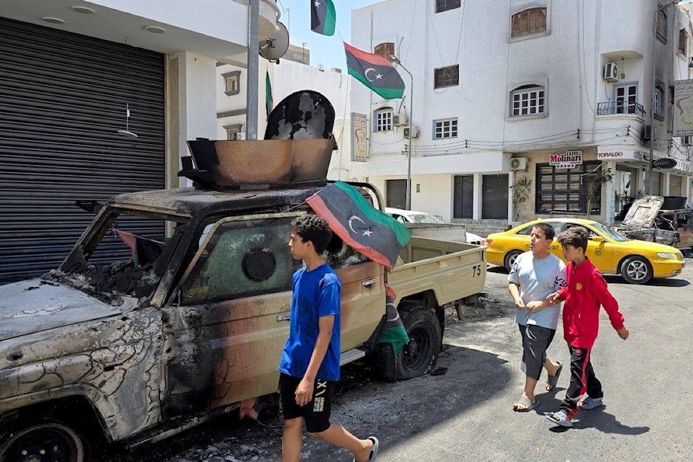 أطفال يمرون بسيارة مدمرة ومحروقة نتيجة الاشتباكات جنوبي طرابلس (13 أيار 2025) (أ ف ب)