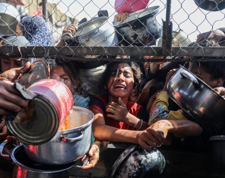 أطفال فلسطينيون يحاولون حصول على حصصهم الغذائية من مطبخ خيري في مخيم للاجئين في خان يونس. قطاع غزة. 30 أيار/مايو 2025 (غارديان)
