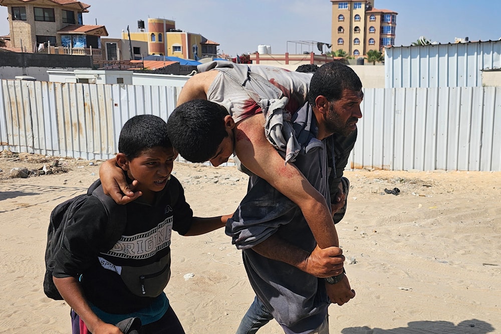 فلسطيني يحمل رجلاً جريحاً أصيب أثناء محاولته الحصول على المساعدات باتجاه مستشفى في رفح جنوبي قطاع غزة - 16 حزيران/يونيو 2025 (أ ف ب)