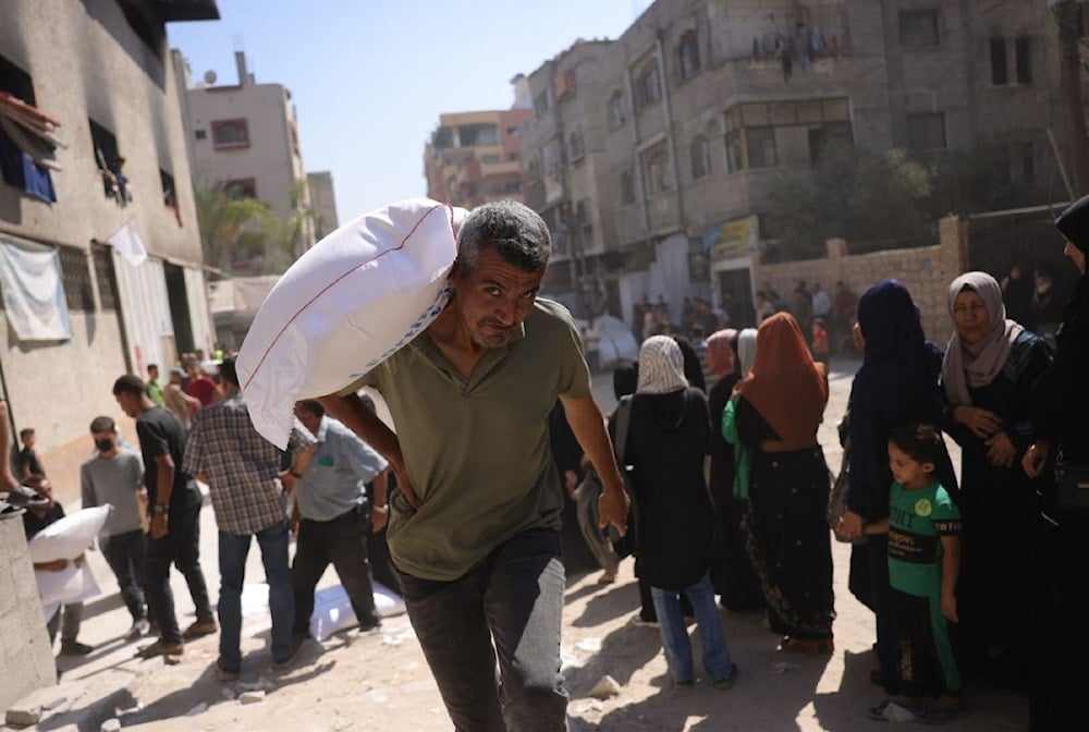 رجل فلسطيني يحمل كيساً من الدقيق بينما ينتظر آخرون أمام نقطة توزيع في مدينة غزة - 26 حزيران/يونيو 2025 (أ ف ب)