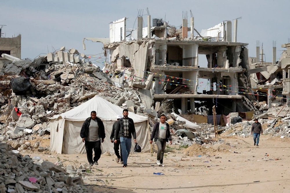 فلسطينيون يسيرون وسط أنقاض المباني التي دمرها الاحتلال الإسرائيلي في رفح جنوب قطاع غزة (رويترز)