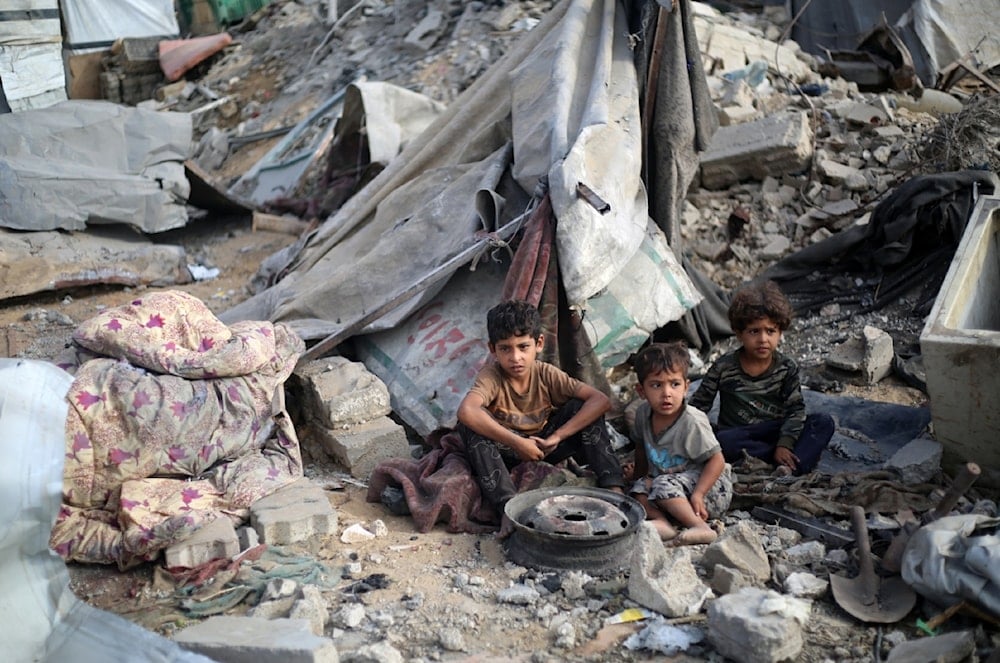 أطفال فلسطينيون يجلسون وسط الدمار في مخيم البريج، وسط قطاع غزة (AFP)