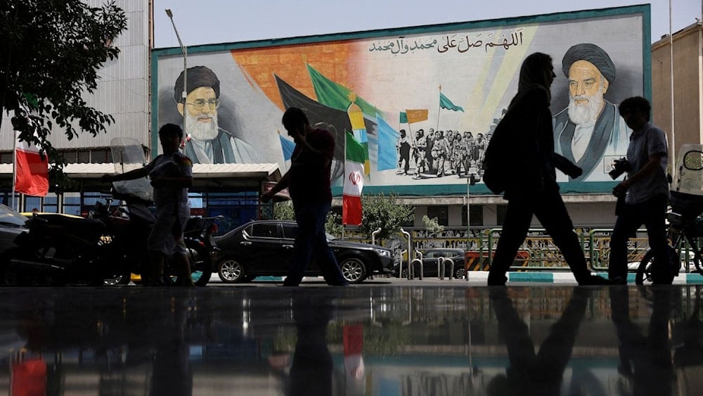 إيرانيون يسيرون بجوار جدارية عليها صورة قائد الثورة والجمهورية الاسلامية في إيران السيد علي خامنئي، والراحل الإمام الخميني