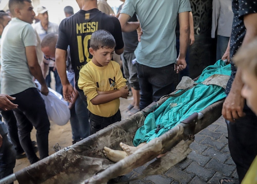 طفل فلسطيني ينظر إلى رجل استشهد بغارات إسرائيلية على مدينة غزة، في 24 آب/أغسطس 2025 (الأناضول)
