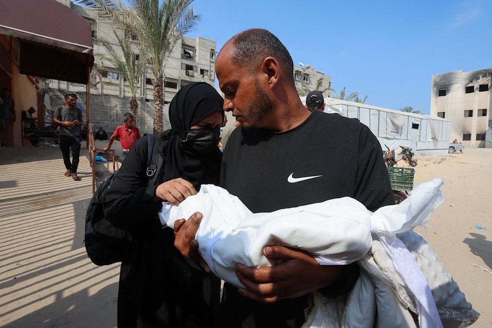 أبٌ وأمٌّ فلسطينيّان يحملان طفلتهما الشهيدة زينب أبو حليب التي توفيت بسبب سوء التغذية في خان يونس جنوبي قطاع غزّة (رويترز)