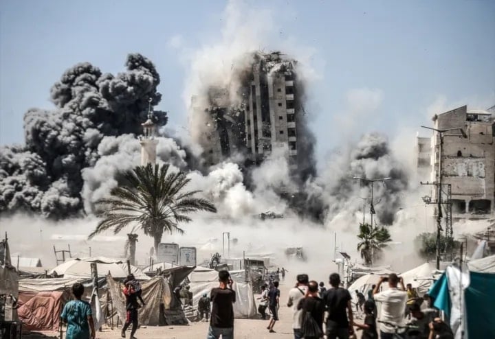 فلسطينيون يشاهدون انفجاراً بعد توجيه الاحتلال الإسرائيلي ضربة عسكرية على برج مشتهى في مدينة غزة (أ ف ب)